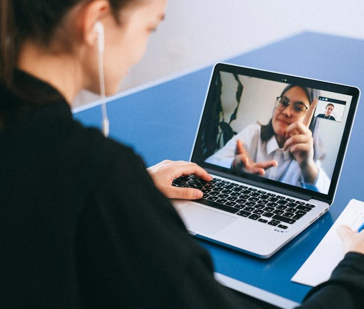 Woman participating in a virtual meeting, taking notes during a video conference on a laptop.