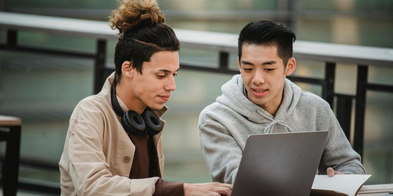 Concentrated multiracial young male students in casual outfits using netbook and notepad while working on project together