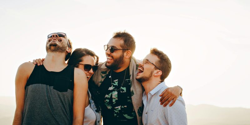 A group of young adults laughing and enjoying time together outdoors under the sun.